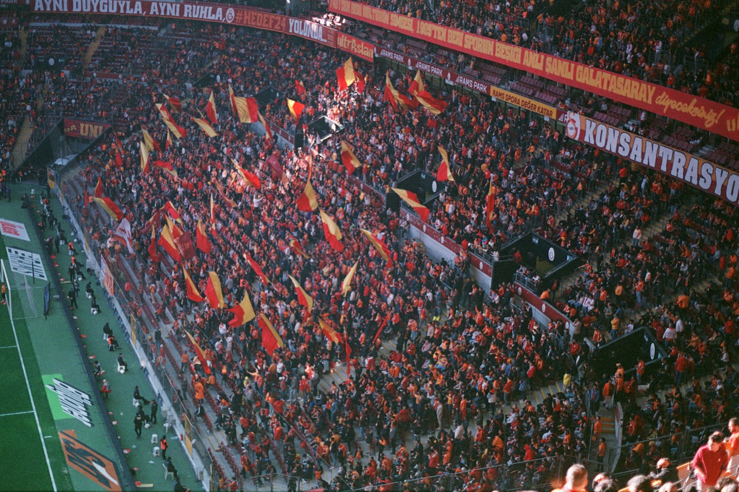 Crowd waves red and yellow flags in a packed stadium.