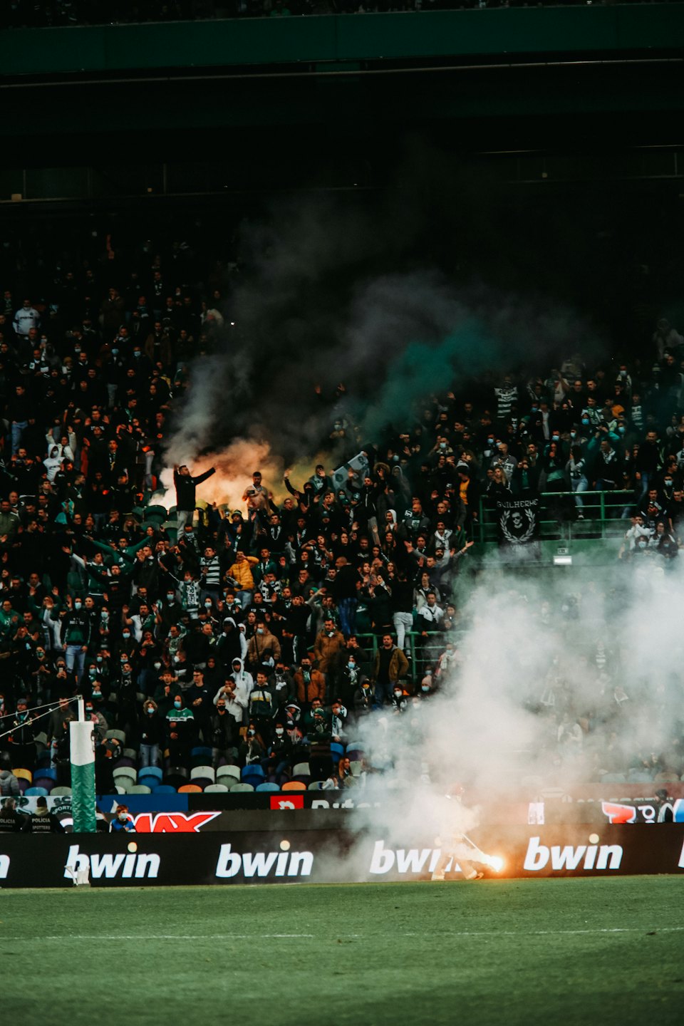 Soccer fans cheer in a stadium with colorful smoke flares.