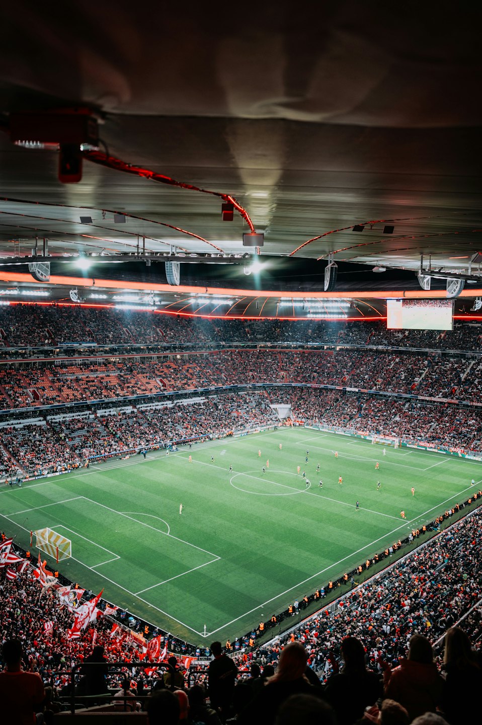 Crowd watches soccer players on a brightly lit stadium field.
